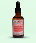 Bild einer braunen Glasflasche mit Pipettenverschluss, die Ohanic Nourishing Oil Serum enthält. Auf dem Etikett steht 'Abyssinian, Argan & Macadamia Oil' sowie 'Cruelty Free, Vegan, 100% Natural Origin'. Das Serum ist frei von Sulfaten, Silikonen, Farbstoffen, Paraffinen und Gluten. Die Flasche hat ein rosa-weißes Etikett mit einem Hinweis auf die natürlichen Inhaltsstoffe.