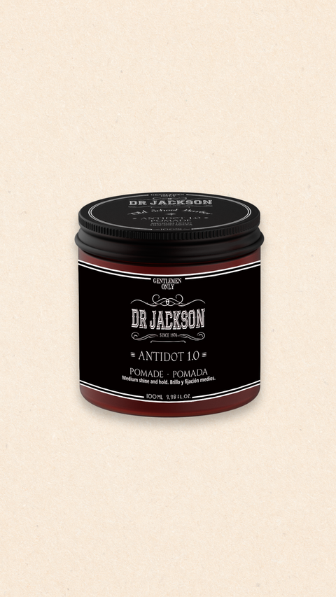 Bild eines 100 ml Behälters von Dr. Jackson Old School Barber Antidot 1.0 Pomade. Der braune Behälter hat ein klassisches Design mit schwarzem Schraubdeckel und weißer Schrift. Die Pomade bietet mittleren Glanz und Halt. Auf dem Behälter steht in mehreren Sprachen 'Pomade Medium Shine and Hold' und 'Pomada Brillo y Fijación Medios'.