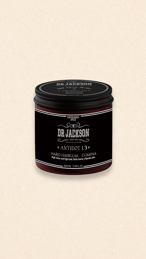 Bild eines 100 ml Behälters von Dr. Jackson Old School Barber Antidot 1.3 Hard Hairgum. Der braune Behälter hat ein klassisches Design mit schwarzem Schraubdeckel und weißer Schrift. Das Haar-Gel bietet starken Halt und hohen Glanz. Auf dem Behälter steht in mehreren Sprachen 'Hard Hairgum High Shine and High Hold' und 'Gomina Brillo Fuerte y Fijación Alta'.